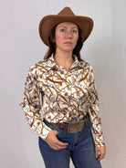 Person wearing a patterned shirt, jeans, and a cowboy hat against a plain background