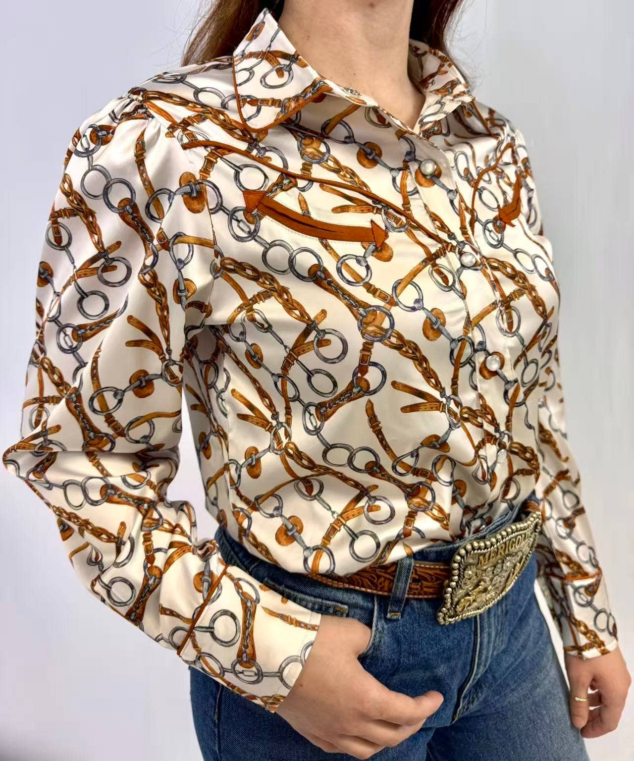 Person wearing a patterned shirt with long sleeves and jeans on a plain background