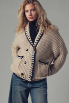 Woman wearing a beige knitted cardigan with black trim on a gray background