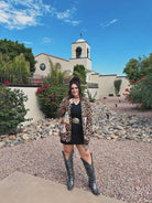 Woman in leopard print jacket and black dress standing in front of a church with a bell tower.