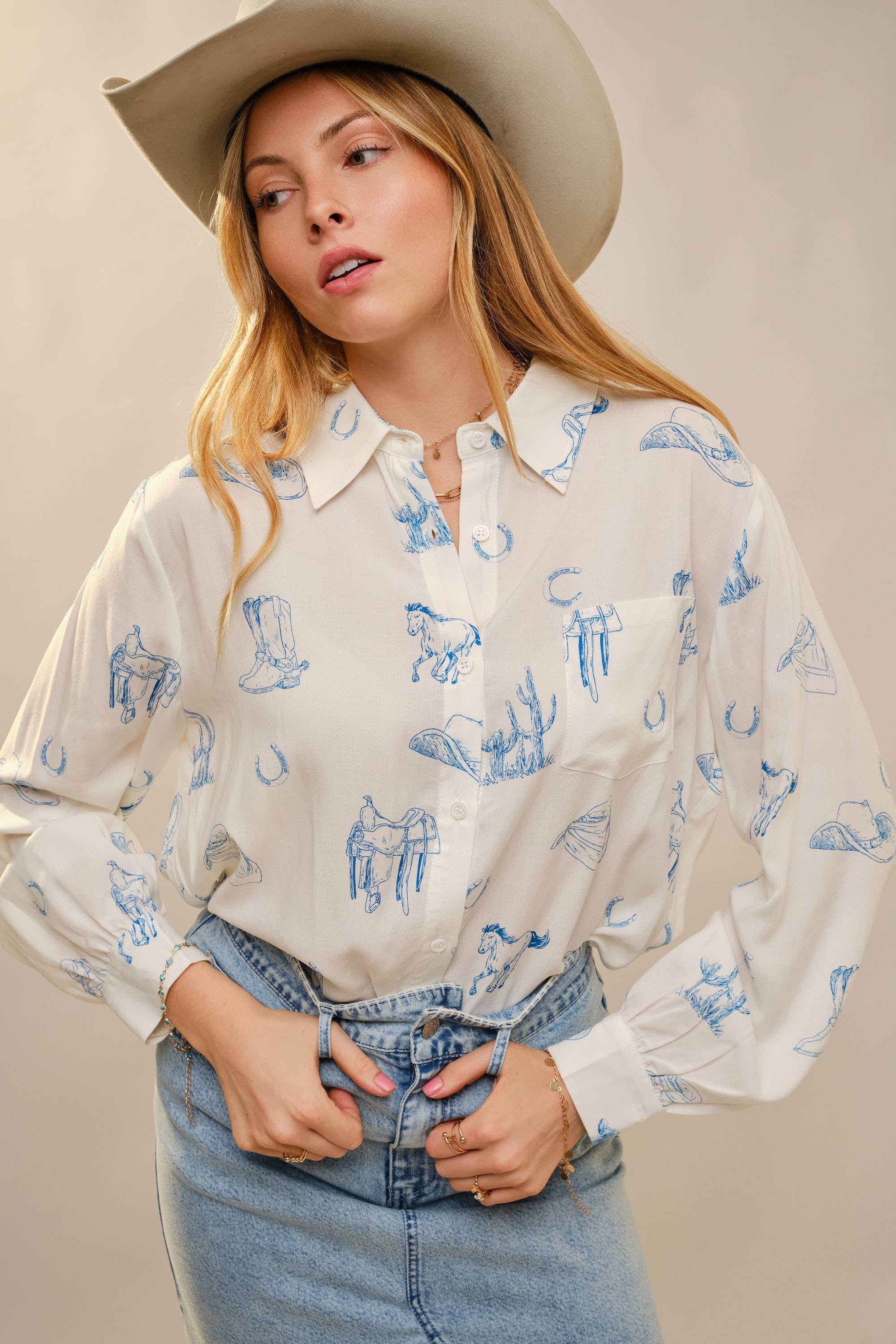 Woman wearing a white blouse with blue patterns and a cowboy hat against a plain background