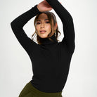 Woman wearing a black turtleneck and green pants against a white background