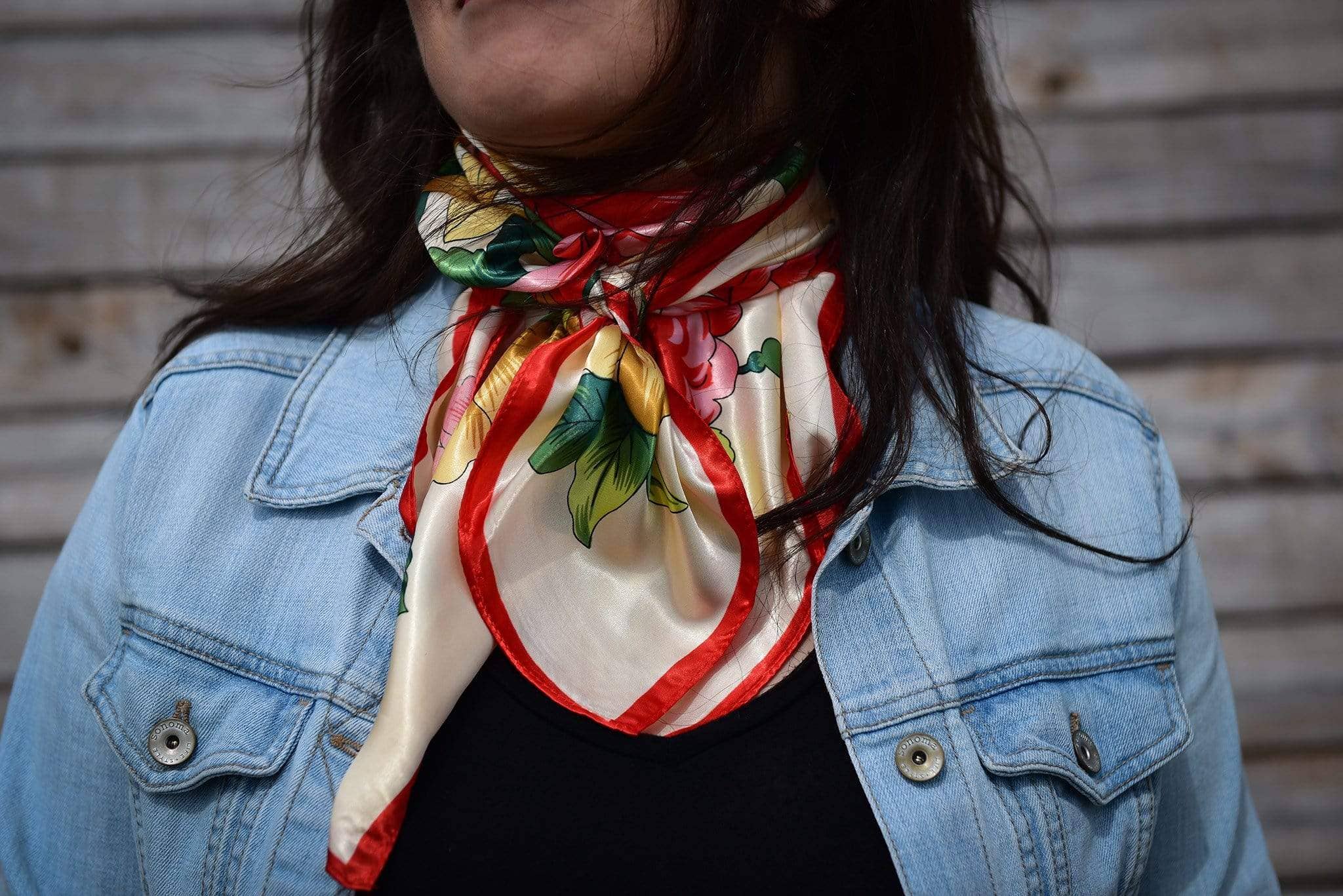 Person wearing a colorful scarf with floral patterns over a denim jacket.