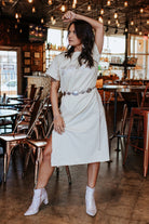 Woman in a white dress posing in a restaurant with wooden floors and tables.