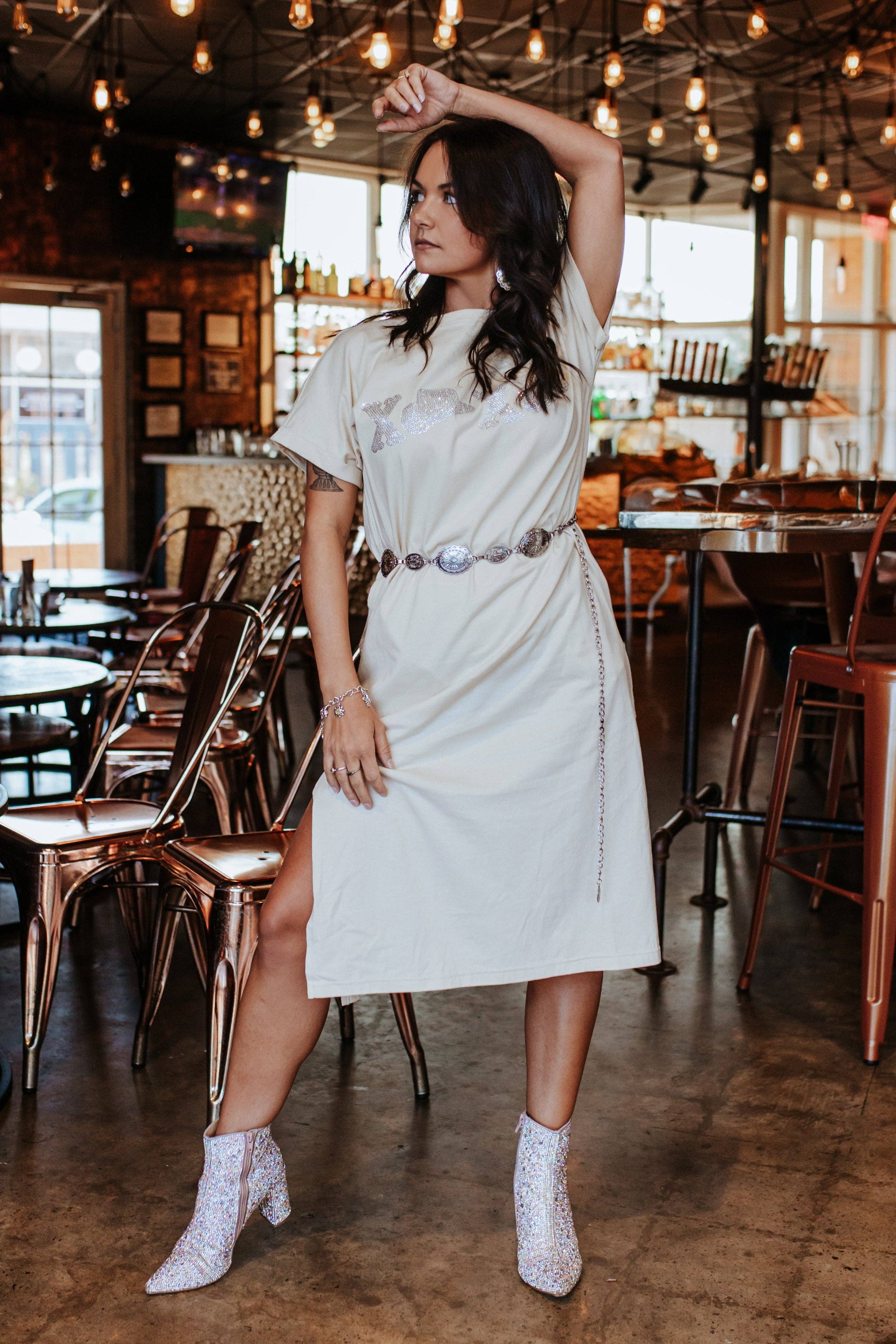 Woman in a white dress posing in a restaurant with wooden floors and tables.
