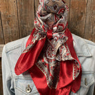 Red and beige patterned scarf draped over a light blue denim jacket against a wooden background