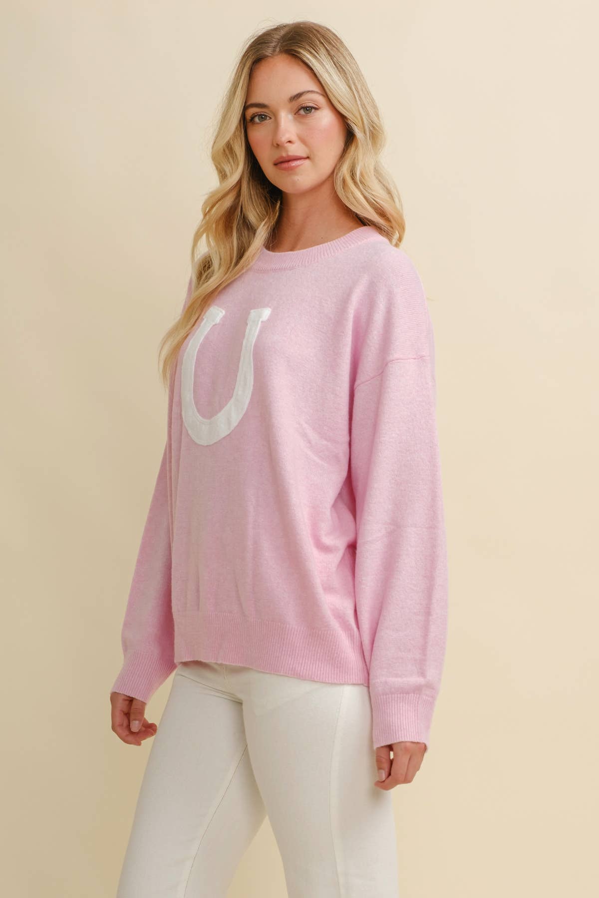 Woman wearing a pink sweater with a large white horse shoe on a beige background