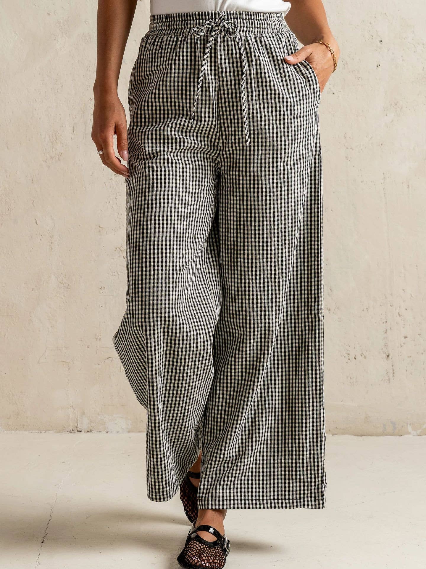 Person wearing black and white checkered pants against a beige wall.