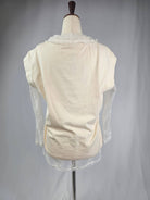 Mannequin wearing a cream-colored garment with sheer sleeves against a plain background