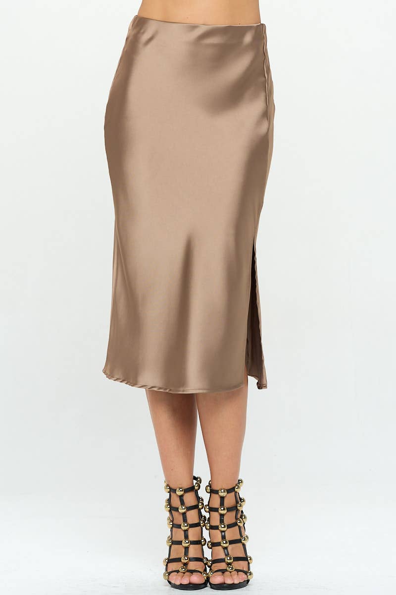 A woman modeling a satin midi skirt with a side slit, in a metallic color, paired with a satin top with a bow detail.