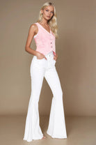 Woman wearing a pink sleeveless top and white flared jeans against a beige background