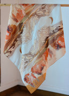 Silk scarf with abstract animal design on a wooden hanger against a white wall.