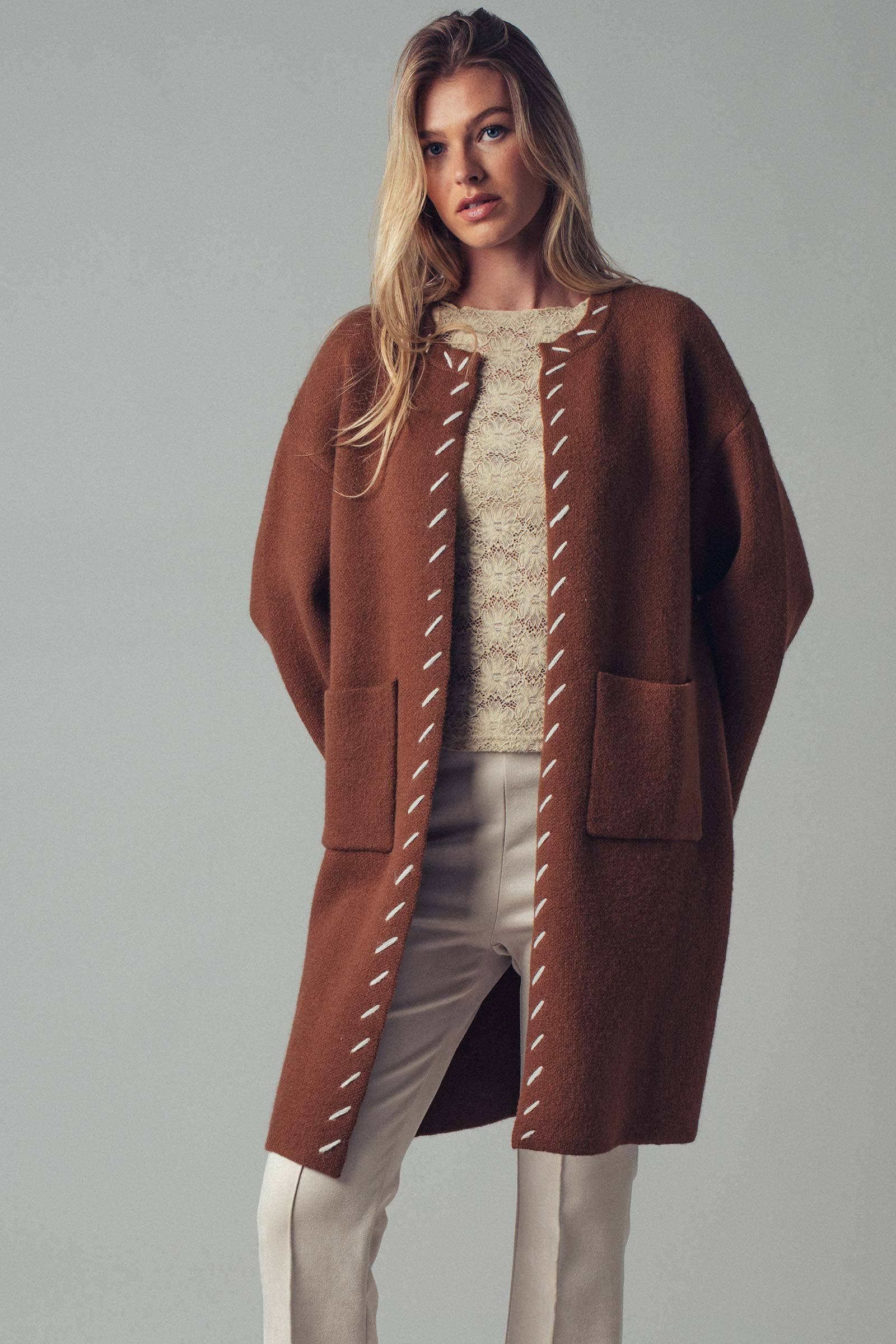 Woman wearing a brown open coat with white bold stitching  trim 