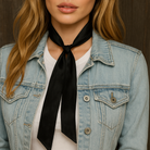 Person wearing a denim jacket with a black scarf around their neck against a dark background