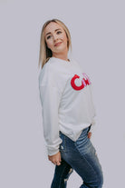 Woman wearing a white sweatshirt with a red logo on a plain background