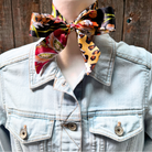 Mannequin wearing a denim jacket with a colorful scarf tied around the neck against a wooden background