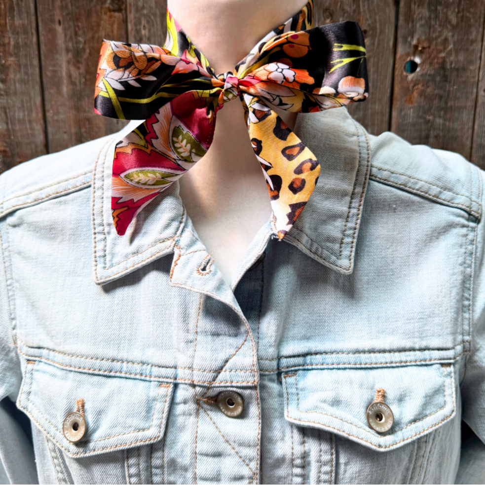 Mannequin wearing a denim jacket with a colorful scarf tied around the neck against a wooden background