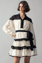 Woman wearing a white dress with black ruffle accents on a gray background