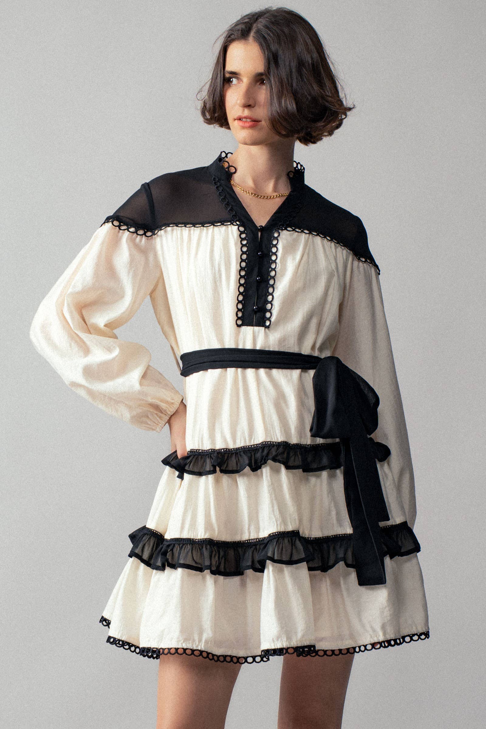 Woman wearing a white dress with black ruffle accents on a gray background