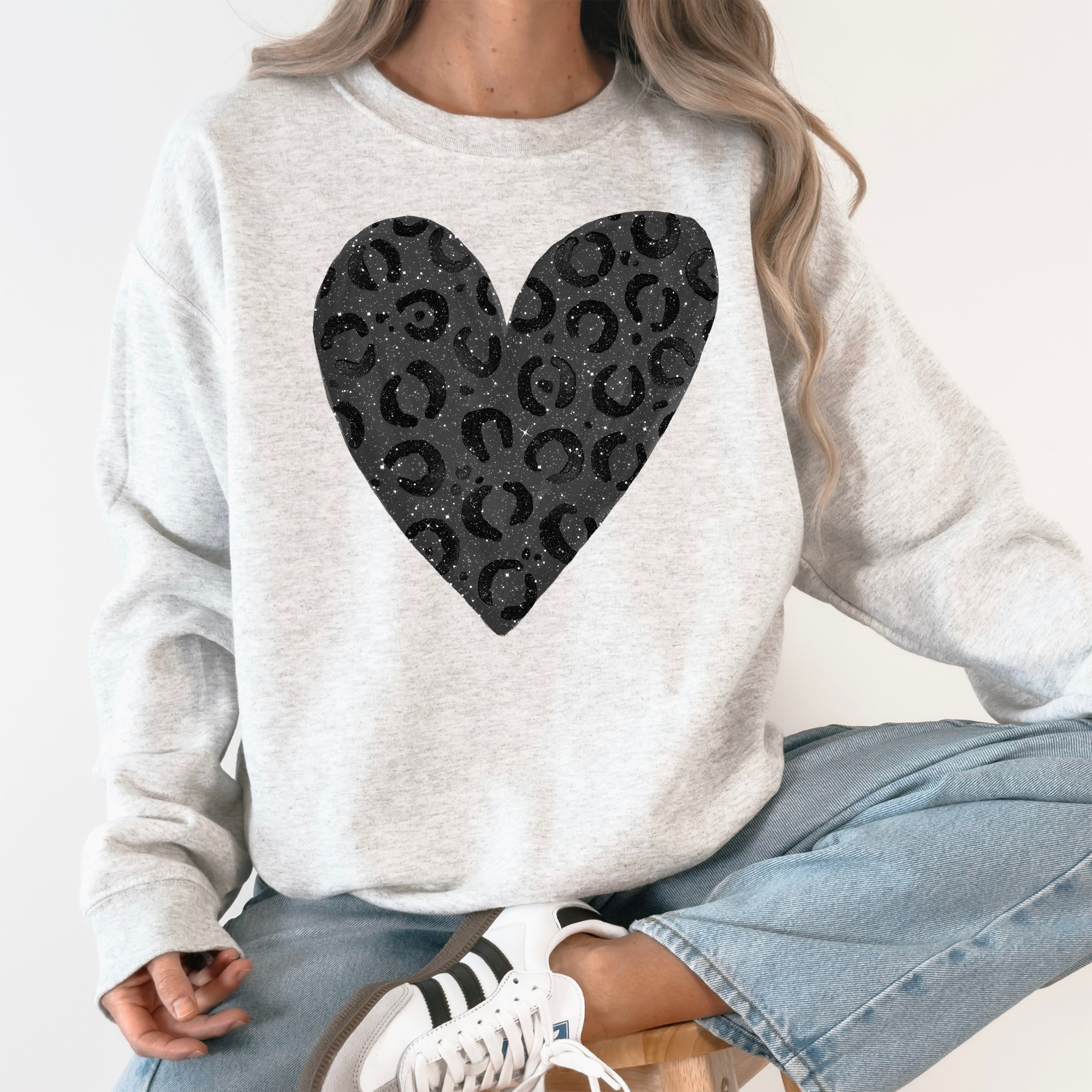 Gray sweatshirt with a black leopard heart-shaped pattern worn by a person sitting on a white surface.