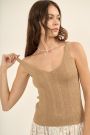 A woman wearing a beige woven tank top with a v-neck cut and fringes at the bottom.