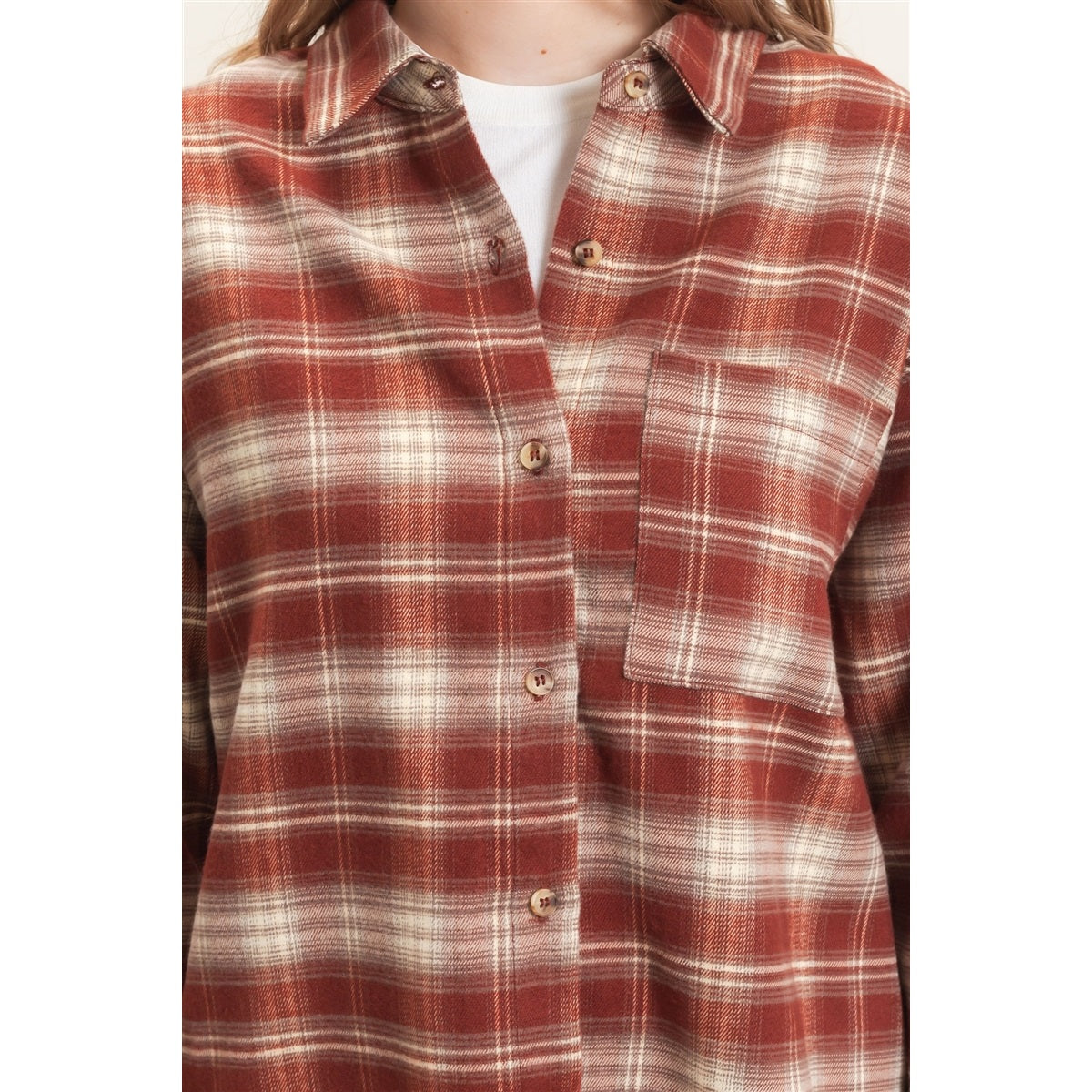 A close-up of a person wearing a rust red and cream plaid button-up shirt over a white undershirt.