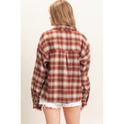 A woman shown from the back wearing an oversized long-sleeve plaid flannel shirt in rust red and cream, paired with white frayed denim shorts, against a plain off-white background.