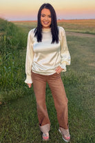 Woman wearing Sand Cat Cuffed Jeans featuring a subtle leopard print, high-rise wide-leg fit, and statement contrast cuff styled with a cream satin blouse.